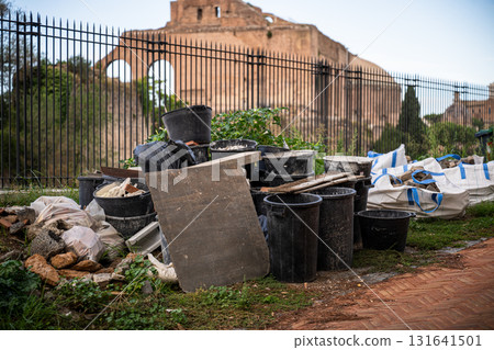 Construction debris and black plastic buckets near ancient ruins and iron fence in Rome 131641501