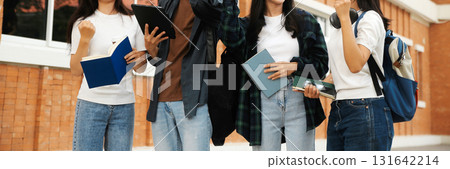 Happy students walking together on university campus, chatting and laughing outdoors after classes 131642214