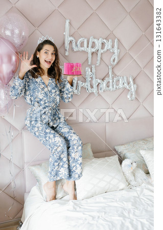 Woman celebrating birthday holding pink cake with balloons and happy birthday sign 131643382