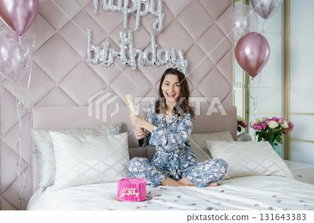 Young woman celebrating birthday opening firecracker on bed Young woman celebrating birthday opening firecracker on bed 131643383