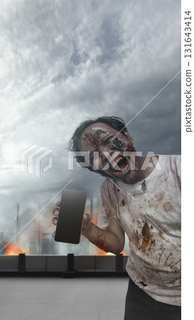 Indonesian southeast asian scary male zombie with a wound and bloody holding a cellphone with an apocalyptic city. Mockup or Copy space. The scene is scary and creepy. Concept of Spooky Halloween 131643414