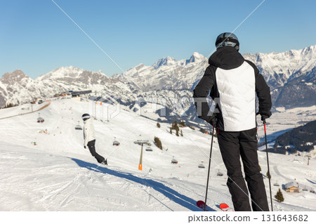 Back view skier standing on snowy slope overlooking Austrian Alps under clear blue sky. Bright winter day filled with crisp air, panoramic mountain views, and peaceful alpine adventure atmosphere 131643682