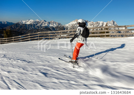 Young adult confident woman skier skiing fast downhill winter alpine skiing resort. Female sporty person with backpack mountain Alps snow slope outdoors cold snowy sunny backlit light day 131643684
