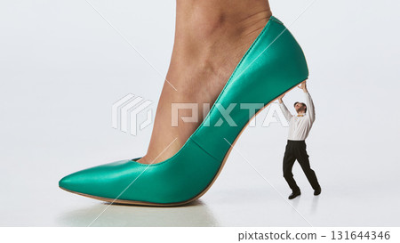 Collage composition. Tiny man holding up towering turquoise stiletto in minimalist power concept 131644346