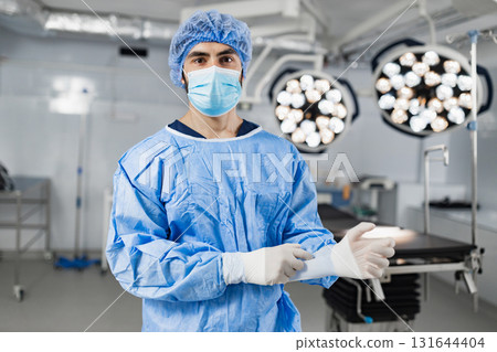 A surgeon wearing a mask and surgical gown prepares for an operation in a modern operating room. A surgeon wearing a mask and surgical gown prepares for an operation in a modern operating room. 131644404