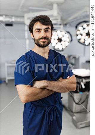 A surgeon stands with arms crossed in an operating room, looking at the camera. 131644443
