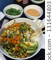Bowl filled with sushi rice, topped with avocado, edamame, corn, and fish roe, surrounded by dipping sauces and green onions, highlighting delicious food presentation 131644803