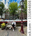 Fashionable woman poses by scenic canal, with bicycles and blooming flowers nearby, showcasing a relaxed urban atmosphere and vibrant lifestyle 131644808