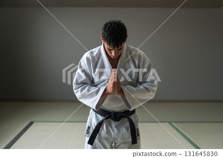 Judo athlete bows respectfully on tatami mat under serene natural light Judo athlete bows respectfully on tatami mat under serene natural light 131645830