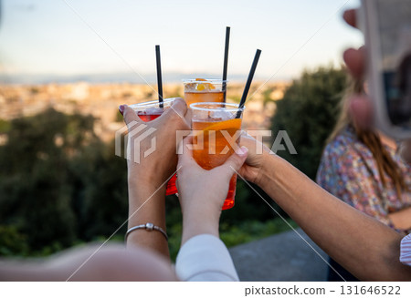 Female hands holding colorful cocktails with orange slice and straw during outdoor celebration Female hands holding colorful cocktails with orange slice and straw during outdoor celebration 131646522