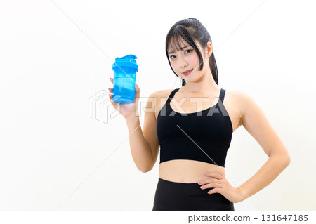 一位訓練有素、酷酷的女士，手裡拿著蛋白搖搖杯。肌肉訓練女孩。白色背景。左邊緣已裁剪。 131647185