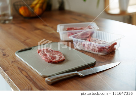 Raw pork steak on cutting board with knife and packaged meat in kitchen 131647336