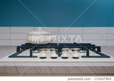 Close-up of a beige gas cooktop with a cast iron grate and a ceramic pot Close-up of a beige gas cooktop with a cast iron grate and a ceramic pot 131647909
