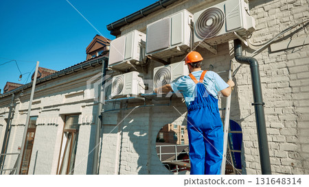 Rear view of technician adjusting outdoor HVAC units on sunny day Rear view of technician adjusting outdoor HVAC units on sunny day 131648314