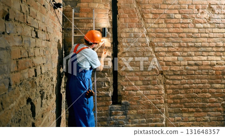 Technician repairing wall light fixture in brick corridor 131648357