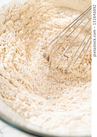 Close-up view of a large glass mixing bowl with flour and a measured amount of spices (including cinnamon and ginger) added on top, ready to be mixed for the Amber Gingerbread Cookie Dough. 131648892