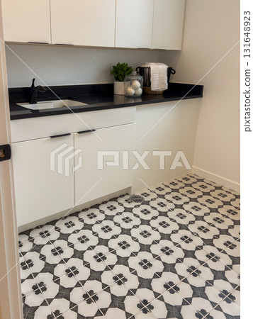 A utility room features black and white patterned tile flooring with white cabinetry and a dark countertop. The space includes a built in sink and minimal decor. 131648923