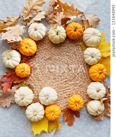 circular arrangement of white and orange mini pumpkins on a woven mat, accented with autumn leaves. A cozy and seasonal setup for fall or Thanksgiving decor. 131648995