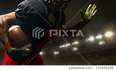Close-up of American football runner holding ball with intensity under 3D stadium lights 131649289