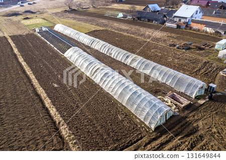 Aerial view of long arched greenhouses covered with polyethylene in plowed spring field. Agriculture and farming. 131649844