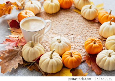 Warm Autumn Morning with Pumpkin Latte. Cup of coffee surrounded by white and orange mini pumpkins with colorful autumn leaves on a woven mat creating a cozy seasonal atmosphere 131649970