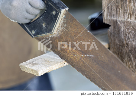 Close up hand saw cutting wood, gloved hand shows texture, rust, and craftsmanship 131651939