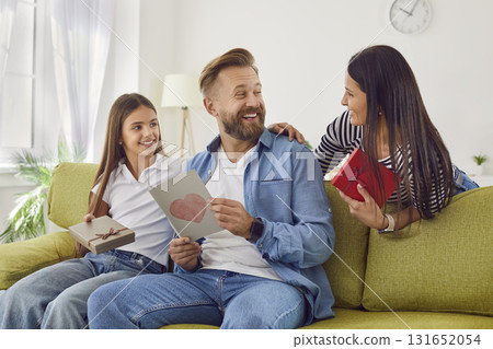 Happy smiling man with greeting card from his wife and daughter sitting on sofa at home. 131652054