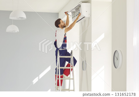 Service worker standing on ladder and repairing something in modern air conditioner 131652178