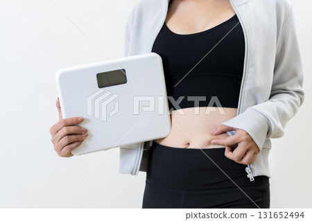 一位女士拿著體重秤,捏著肚子。一位酷酷的女士正在健身。正在減肥。白色背景。已修剪。 一位女士拿著體重秤,捏著肚子。一位酷酷的女士正在健身。正在減肥。白色背景。已修剪。 131652494