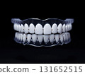 A close-up shot of a dental teeth model, showcasing perfect white teeth and a clear retainer, set against a dark backdrop. 131652515