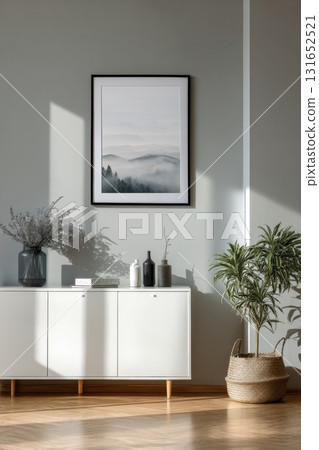 Modern interior with a framed artwork on a gray wall above a white cabinet, decorated with vases, plants, and natural sunlight Modern interior with a framed artwork on a gray wall above a white cabinet, decorated with vases, plants, and natural sunlight 131652521
