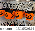Orange felt buckets with jack o lantern faces and black handles on retail display. Halloween container, candy collection, seasonal festivity, tradition, playful celebration and autumn folklore. 131652684