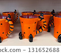 Orange ceramic mugs with witch legs and striped handles on store shelf. Halloween decoration, seasonal festivity, tradition, holiday merchandise, quirky design and spooky culture. 131652688