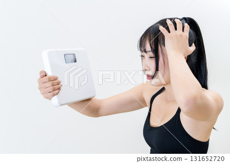 一位女士手持體重秤，托著頭。一位酷酷的女士正在健身。正在節食。白色背景。 131652720