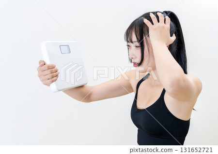 A woman holding a weight scale and holding her head. A cool woman working out. Diet. White background. 131652721