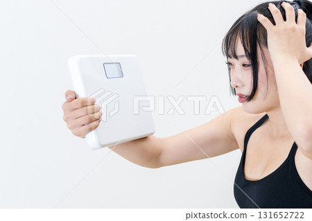 Woman holding a weight scale and holding her head. A cool woman working out. Diet. White background. Trimmed. 131652722
