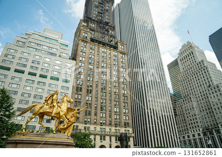 A striking view of the gilded William Tecumseh Sherman statue at Grand Army Plaza in New York City. Tall skyscrapers rise behind the monument under a bright summer sky, blending history and modern 131652861