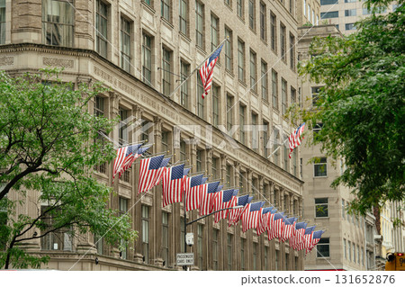 Multiple American flags are displayed in rows along the facade of a historic New York City building. The scene highlights patriotism and classic architecture surrounded by green trees in a downtown 131652876