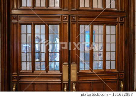 A close-up view of the lower section of a Gothic wooden door with multiple glass panels. The rich wood texture and symmetrical design reflect traditional craftsmanship. 131652897
