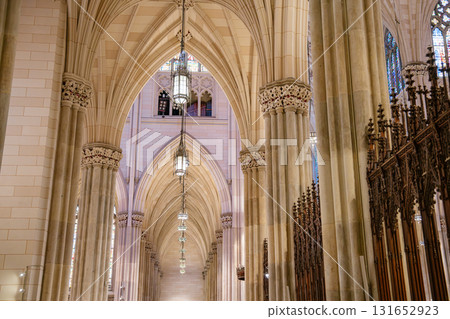 This image highlights a corridor of pointed arches, hanging lanterns, and stone columns inside St. Patrick's Cathedral in New York City. The Gothic Revival design is accentuated by soft light and 131652923