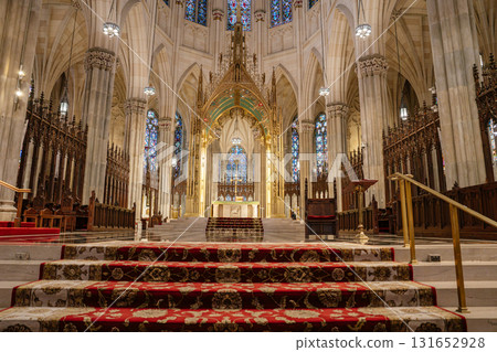 The image captures the grand main altar of St. Patrick's Cathedral in New York City, framed by golden Gothic arches and stained glass windows. Ornate columns, carved woodwork, and rich red carpets The image captures the grand main altar of St. Patrick's Cathedral in New York City, framed by golden Gothic arches and stained glass windows. Ornate columns, carved woodwork, and rich red carpets 131652928