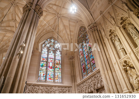 The photo shows vibrant stained glass windows and detailed stone statues inside St. Patrick's Cathedral in New York City. The elegant Gothic architecture includes high columns, pointed arches, and The photo shows vibrant stained glass windows and detailed stone statues inside St. Patrick's Cathedral in New York City. The elegant Gothic architecture includes high columns, pointed arches, and 131652930