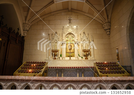 A marble altar showcases a holy image of Christ's face at the center, surrounded by intricate carvings and golden candlesticks. Rows of votive candles glow warmly on both sides, inviting prayer and 131652938