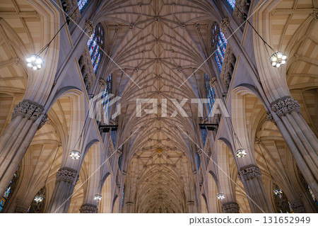 An upward view reveals the ornate gothic ceiling of St. Patrick's Cathedral in New York City. The pointed arches, carved columns, and stained glass windows highlight the architectural elegance. 131652949