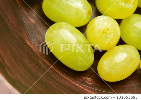 Close-up of freshly picked green nutritious seedless grapes in a wooden bowl Close-up of freshly picked green nutritious seedless grapes in a wooden bowl 131653685