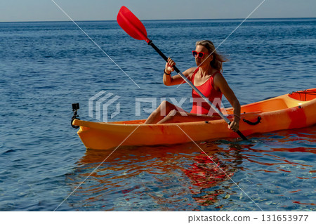 Kayaking, woman, ocean. A woman paddling an orange kayak on the clear blue ocean, enjoying an active summer vacation Kayaking, woman, ocean. A woman paddling an orange kayak on the clear blue ocean, enjoying an active summer vacation 131653977