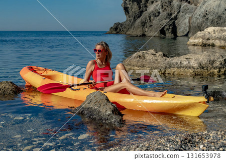 Kayak, woman, ocean. Woman relaxing in a yellow kayak on a rocky ocean shore, enjoying summer leisure 131653978