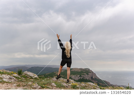 A woman stands on a mountain top, arms raised in the air A woman stands on a mountain top, arms raised in the air 131654020