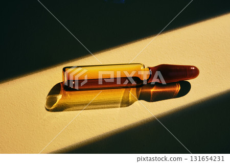 A ampoule of a cosmetic preparation in a beam of light on a beige background. 131654231