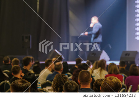 Crowd attends a conference as a speaker delivers a presentation on stage to audience Crowd attends a conference as a speaker delivers a presentation on stage to audience 131654238